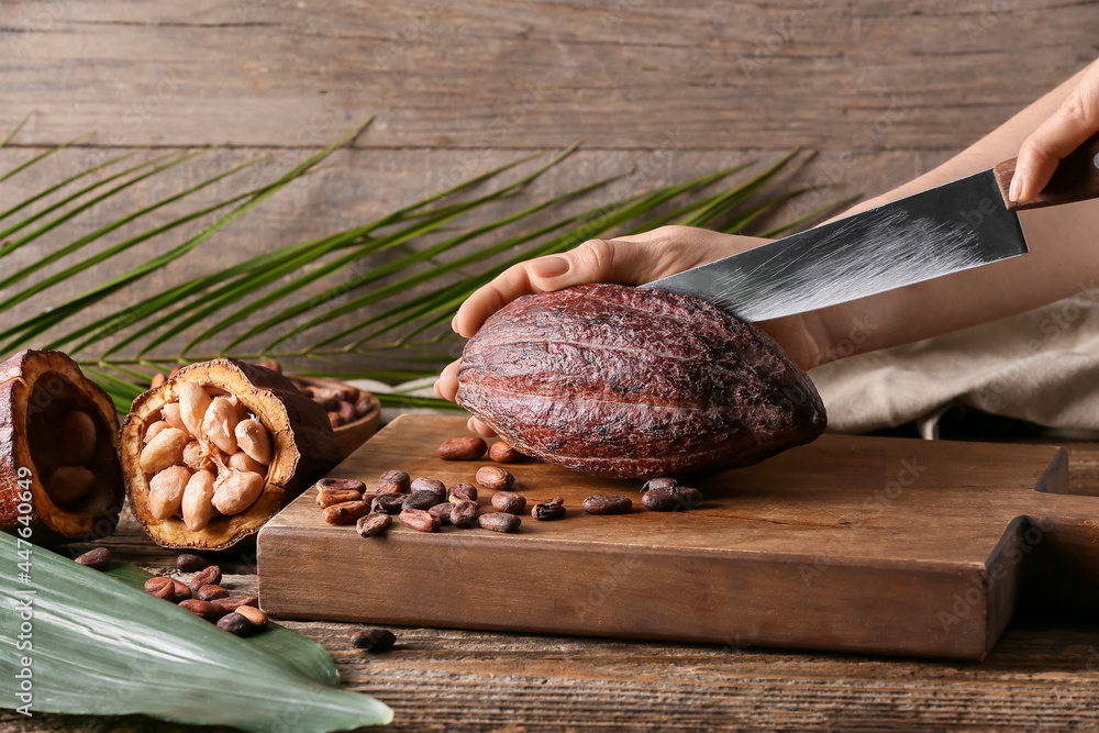 Woman cutting fresh cocoa fruit on wooden background