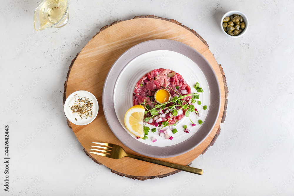 Plate with tasty beef tartare and sauce on light background