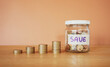 © tendo23 - Stack of money coin and coin in a glass jar on wooden desk with brown background, Saving money concept
