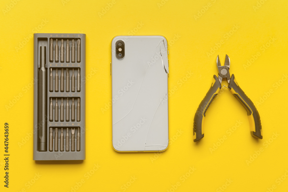 Damaged mobile phone with technician tools on color background