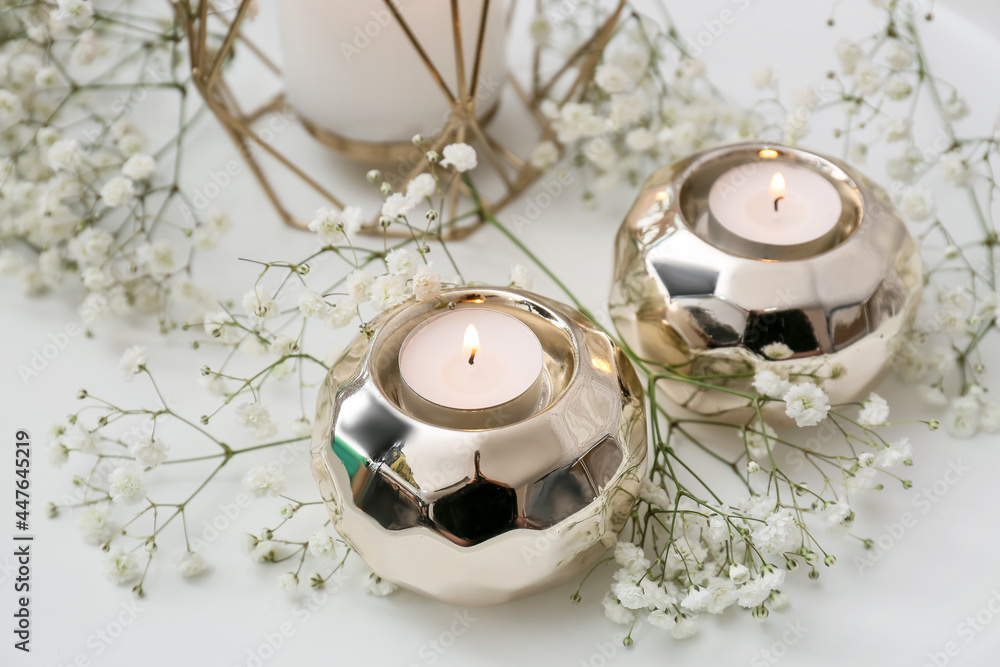 Beautiful gypsophila flowers and burning candles on light background