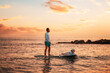© _KUBE_ - Family summer vacations. Father and daughter surfing on a sup board. Sunset sky and sea of peach color at the background. Copy space