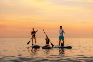 Group of caucasian people swimming on a sup boards at the ocean. Sport activity of friends at the vacation. Summer sport and recreation. Copy space