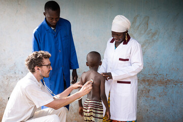 white medical volunteer auscultating the lungs of a skinny little african boy under the supervision 