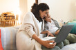 © Wavebreak Media - Smiling mixed race mother and daughter sitting on sofa, using laptop and tablet