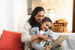 © Wavebreak Media - Smiling mixed race mother and daughter sitting on sofa, using tablet