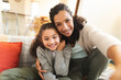 © Wavebreak Media - Smiling mixed race mother and daughter sitting on sofa having video call