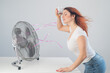 © Михаил Решетников - A red-haired Caucasian woman chills by the electric fan and drinks a cold drink. Climate control in the apartment