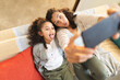 © Wavebreak Media - Mixed race mother and daughter sitting on sofa doing funny faces, taking selfie