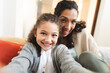© Wavebreak Media - Mixed race mother and daughter sitting on sofa doing funny faces, taking selfie