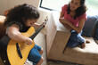 © Wavebreak Media - Mixed race mother and daughter sitting on sofa and playing guitar