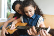 © Wavebreak Media - Mixed race mother and daughter sitting on sofa and playing guitar