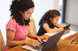 © Wavebreak Media - Mixed race mother and daughter sitting at table, using laptop and tablet