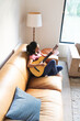 © Wavebreak Media - Mixed race woman sitting on sofa and playing guitar