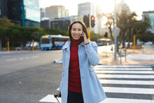 Portrait Of Asian Woman Using Smartphone And Crossing Road With Suitcase