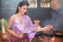 Beautiful Asian Woman Wearing Traditional Thai Dress. She Was Cooking In The Old Wooden House Kitchen. In The Concept Of Retro Lifestyle Of Ayutthaya People In The Past