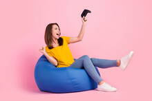 Photo Of Excited Lucky Woman Dressed Yellow T-shirt Sitting Bean Bag Holding Playstation Rising Fist Isolated Pink Color Background