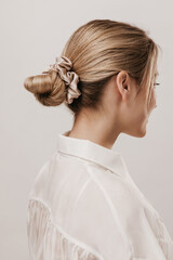 portrait of stylish blonde with hair collected in silk beige scrunchie, wearing white blouse and pos