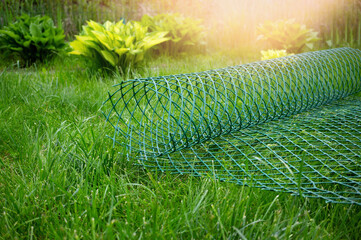 roll of plastic green mesh for the garden lies on the lawn. garden net for fixing plants and fencing is ready for work