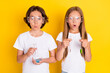 Portrait of two attractive amazed cheerful schoolkids making experiment isolated over bright yellow color background