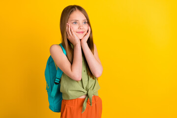 Photo portrait schoolgirl wearing green shirt rucksack looking blank space touching cheeks isolated bright yellow color background