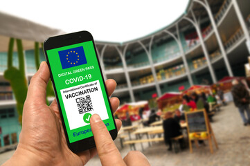 Wall Mural - A man in a shopping mall holds a smartphone with the European Union digital green pass for Covid-19 in his hand. Safety concept for Coronavirus and the Green pass