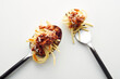 Top view of a fork and spoon with spaghetti bolognese in the light background