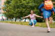© skif - loving family. caring mother meets cheerful children, boy and girl with backpacks running in her arms, meeting children hugging them, after school classes in park. Back to school. first day training