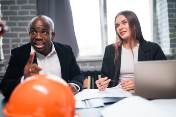 Wall Mural - African American businessman and businesswoman are sitting in negotiations at the table with a construction helmet lying on it