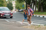 Fototapeta Łazienka - girl and boy with backpacks carefully cross road on pedestrian crossing on their way to school. Traffic rules. Walking path along zebra in city. concept of pedestrians crossing pedestrian crossing.
