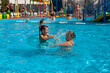 © Юля Бурмистрова - Grandmother and granddaughter in the pool. Cheerful grandmother and granddaughter splash water drops in the pool of the water park on a sunny day, weekend activity.