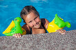 A girl with armbands. A beautiful, cute girl in inflatable armbands holds on to the diving board of the pool on a sea trip. 