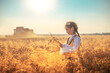 © ValentinValkov - Young girl in traditional Bulgarian folklore costume at the agricultural wheat field during harvest time with industrial combine machine
