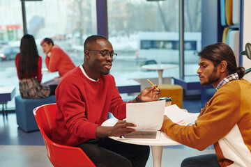 Poster - Two young contemporary intercultural businessmen in casualwear looking at paper