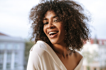 Canvas Print - Joyful girl in white cool shirt smiling on terrace. Modern woman with short curly hairstyle looking into camera on balcony..