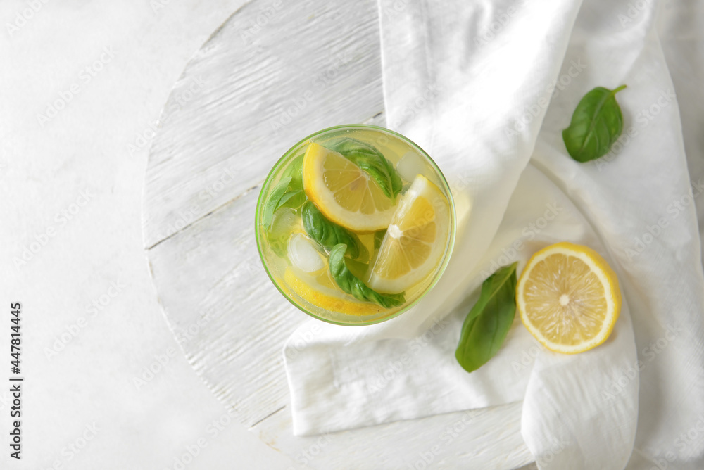 Glass of tasty lemonade with basil on light background