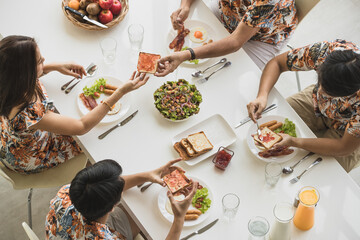 Top, aerial view Asian family sitting and having breakfast, bread with jam, taking care of each other in a bright refresh morning at table in comfortable dining room at home with happiness and warmth.