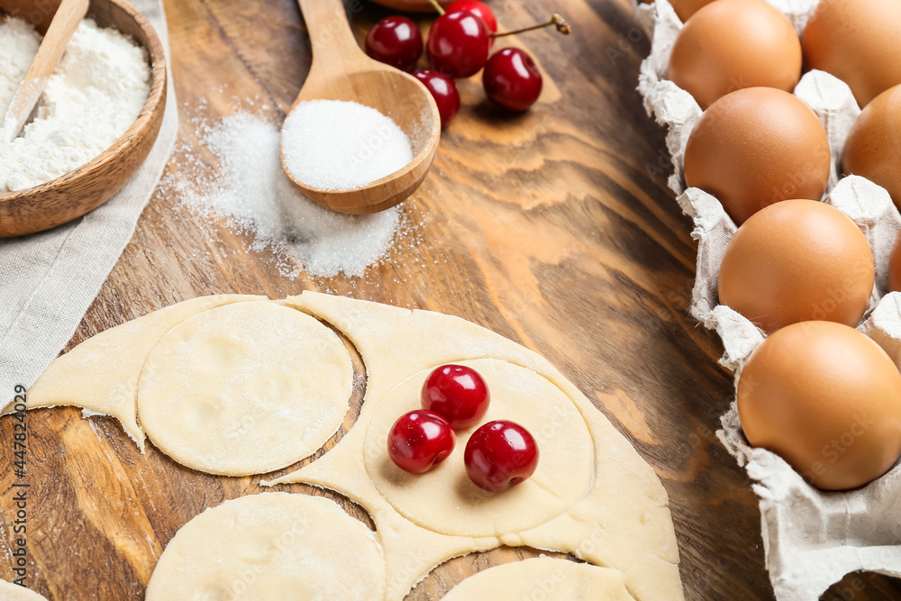 Fresh dough for cherry dumplings and ingredients on wooden background