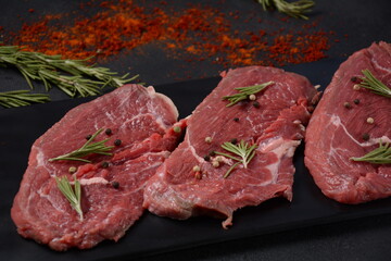 Three pieces of traditional thin steak cut from the tenderloin on wooden cutting board with olive oil, salt, rosemary and pepper. Raw Black Angus Prime meat steaks suitable for grilling on frying pan.