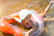 © Ольга Симонова - Girl in a hat swimming in the river with a transparent inflatable circle in the shape of a heart with orange feathers inside.The sea with a sandy bottom. Beach holidays, swimming, tanning, sunscreens.
