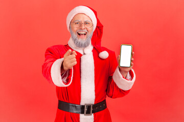 Wall Mural - extremely happy elderly man with toothy smile wearing santa claus costume and red hat pointing to ca