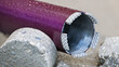 Closeup of wet purple core drill bit and cylindrical bored piece of gray concrete tile. Drilling hole saw tool with crown of diamond grit embedded in metal segments on cutting edge. Civil engineering.