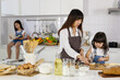 © Bangkok Click Studio - Asain lovely family, mom and two little daughters cooking and playing in modern kitchen. The younger sister learning how to make a bakery or bread while the elder sitting on counter and reading book