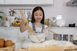 © Bangkok Click Studio - A little cute long black fair hair Asian girl, 7 years old, learning how to make bread and bakery with a curious and happy smile face. She learns and plays with flour in a bowl in modern kitchen