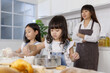 © Bangkok Click Studio - Two little cute Asian girls, 3 years and 7 years old, learning how to make bread and bakery with a curious and happy smiley face. Their mom standing and looking behind them
