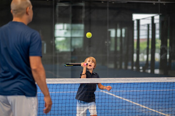 Monitor teaching padel class to child, his student - Trainer teaches little boy how to play padel on indoor tennis court