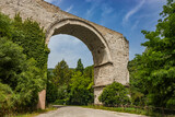 The ruins of the Roman arch bridge of Augustus, in Narni, Terni, Umbria. The remains of the bridge over the Nera river. The big and ancient stone arch, against the blue sky. Trees and dense vegetation