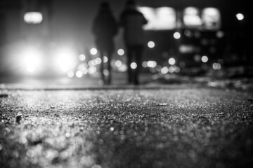 Wall Mural - Rainy night in the big city, glare from the headlights of the car parked and people passing near. Close up view from the sidewalk level