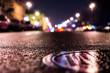 Wall Mural - Rainy night in the big city, the headlights of the approaching cars on the road. Close up view of a hatch at the level of the asphalt