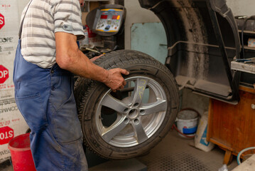 Car mechanic balancing car wheel on a computer machine balancer in auto repair service.